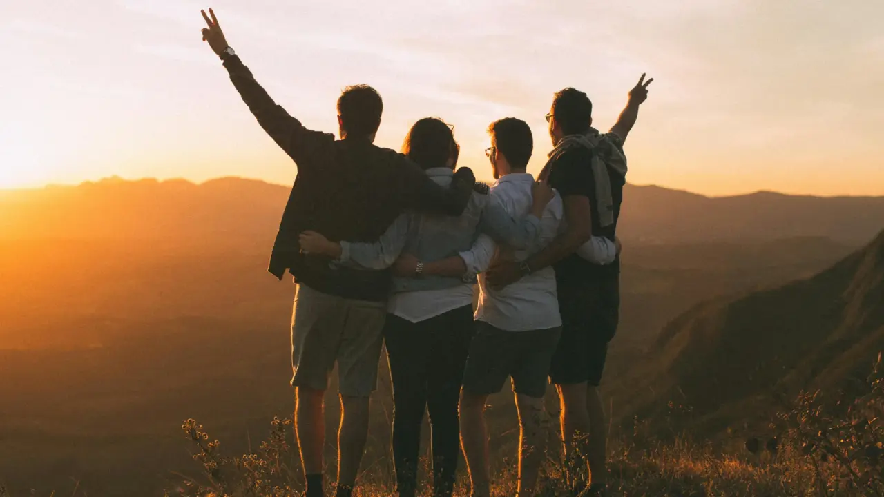 Eine Gruppe junger Menschen hält sich in den Armen und blickt zusammen auf den Sonnenuntergang